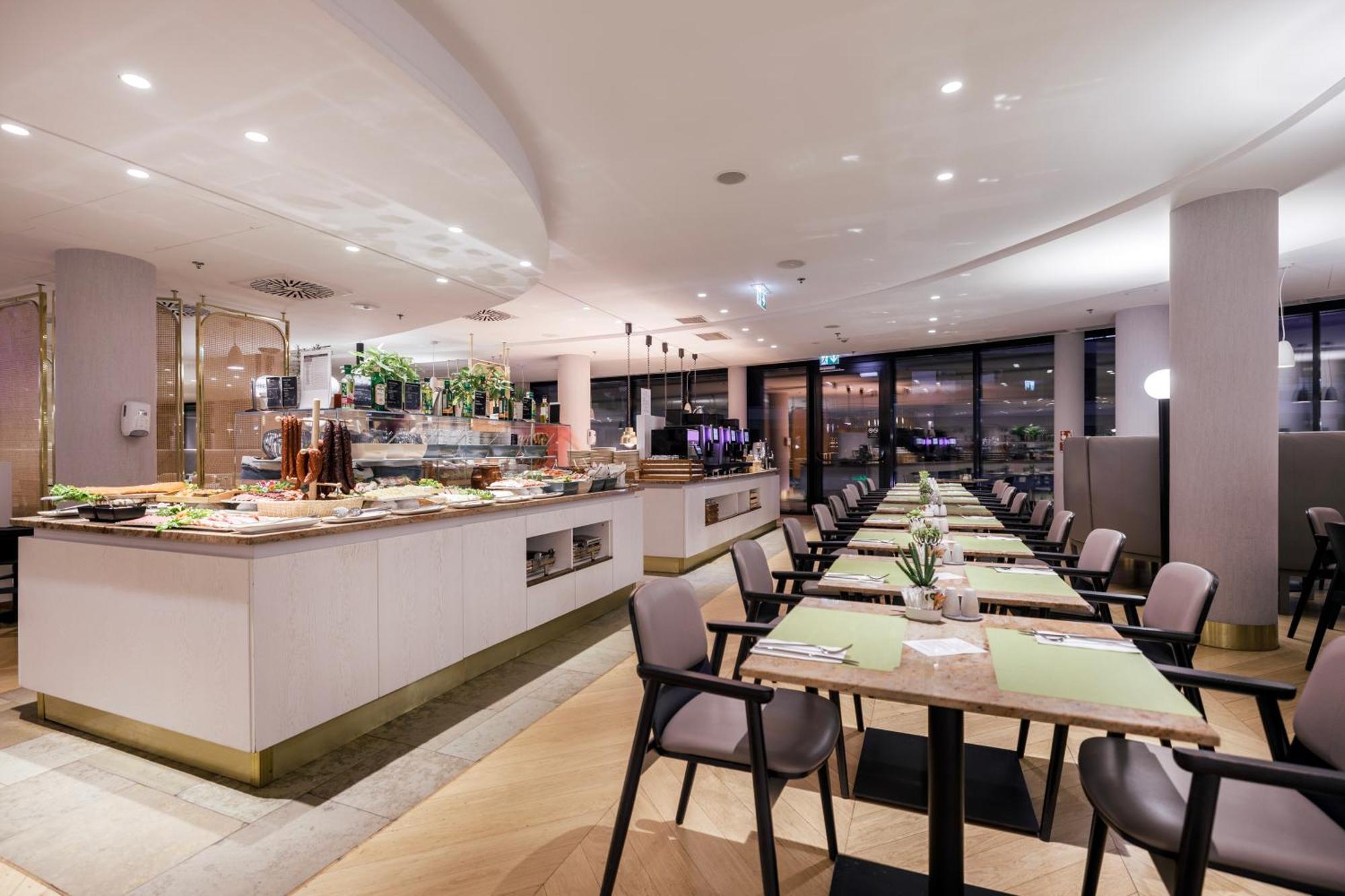 Radisson Blu Resort 슈비노우이스쳬 외부 사진 The photo shows a modern restaurant interior. There is a long dining table set with green placemats, and several chairs arranged around it. To the left, there is a buffet area featuring a variety of dishes and drinks, beautifully presented. The resta