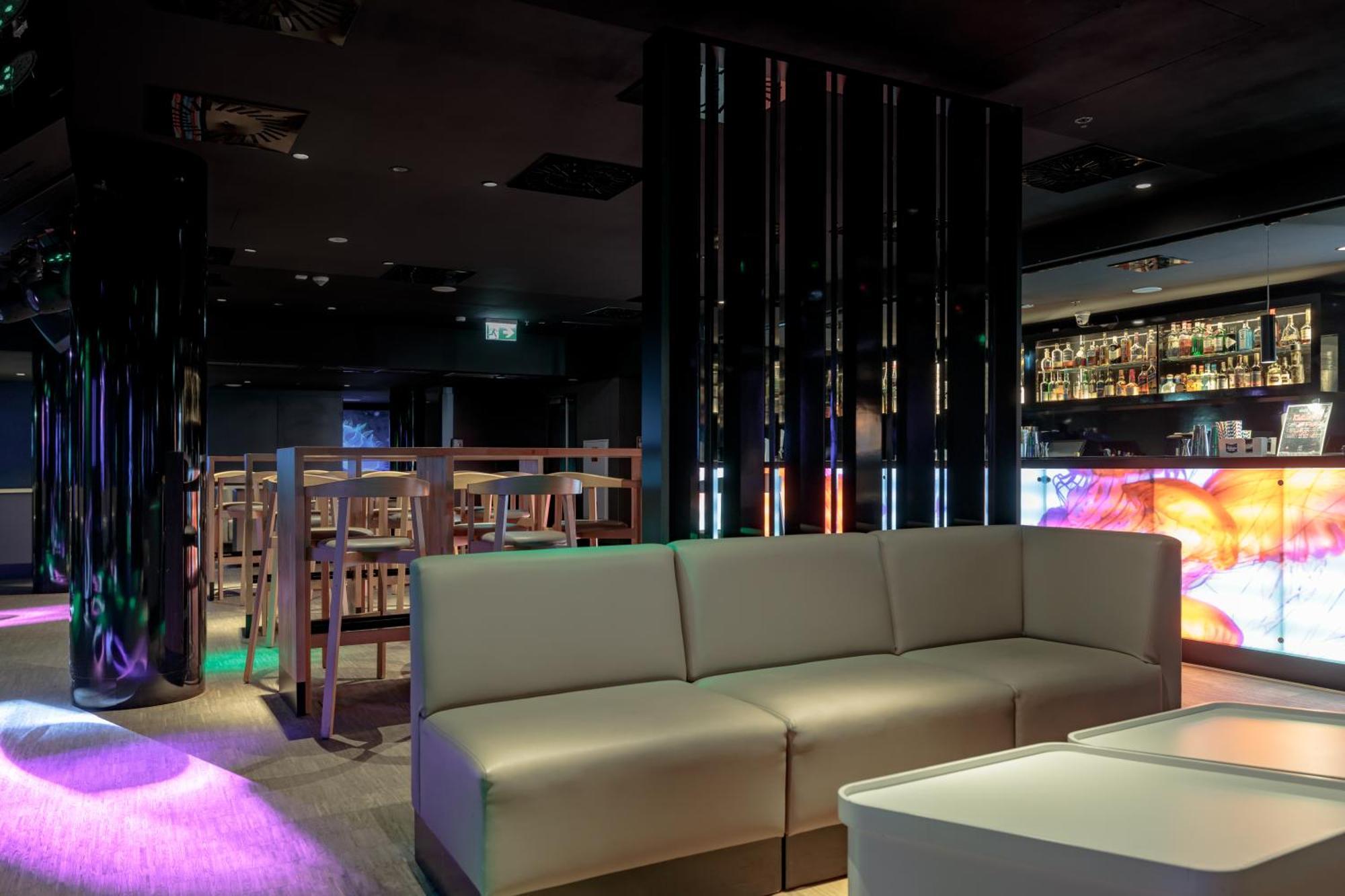 Radisson Blu Resort 슈비노우이스쳬 외부 사진 The photo shows the interior of a stylish lounge or bar. The space features a modern design with dark walls and a sleek atmosphere. There is a beige sectional sofa in the foreground, providing a casual seating area. In the background, a bar is visibl