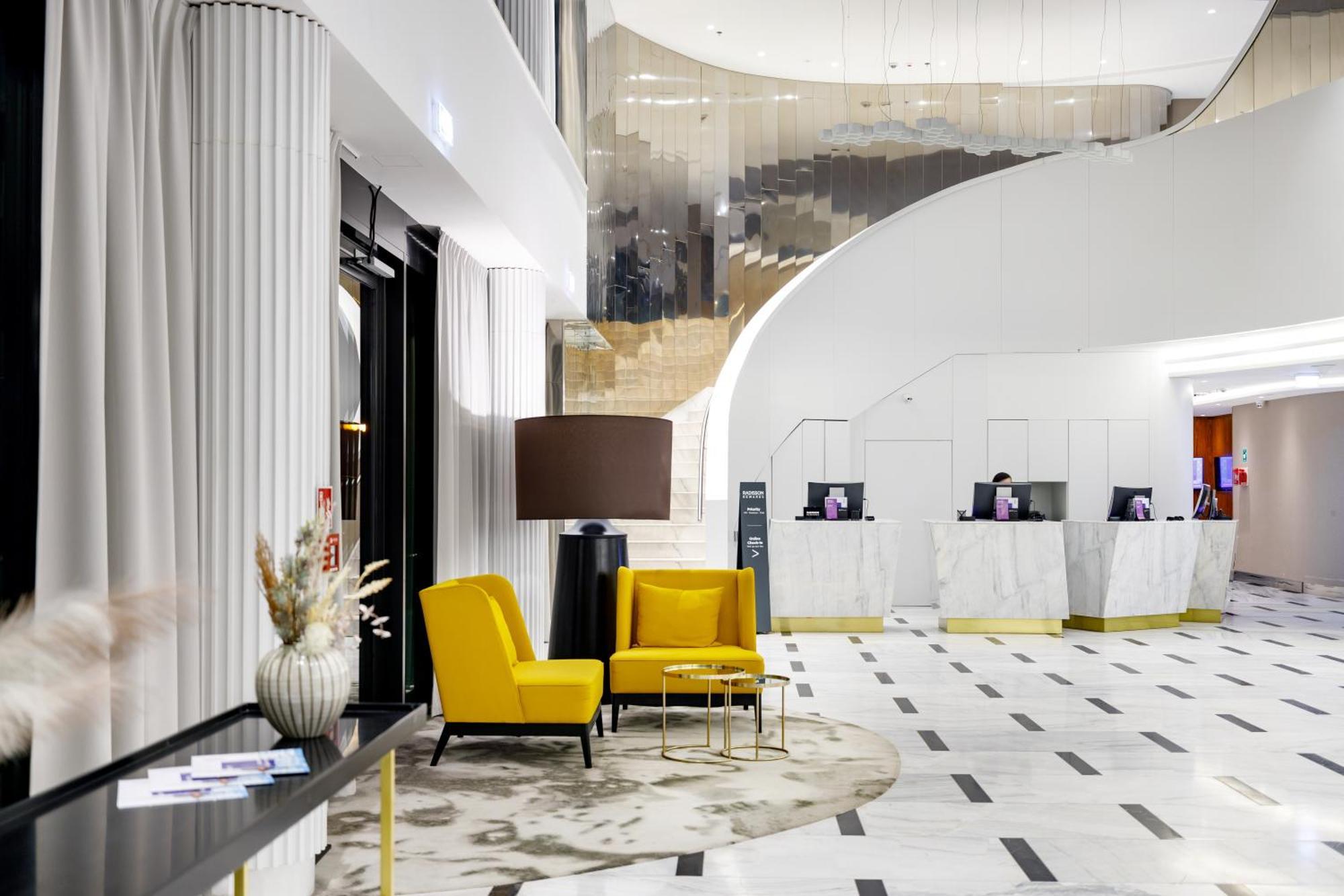 Radisson Blu Resort 슈비노우이스쳬 외부 사진 The photo shows the interior of a modern hotel lobby. The space features a stylish design with a combination of yellow and neutral-colored seating, including two yellow armchairs and a small table. In the background, there is a reception area with ma