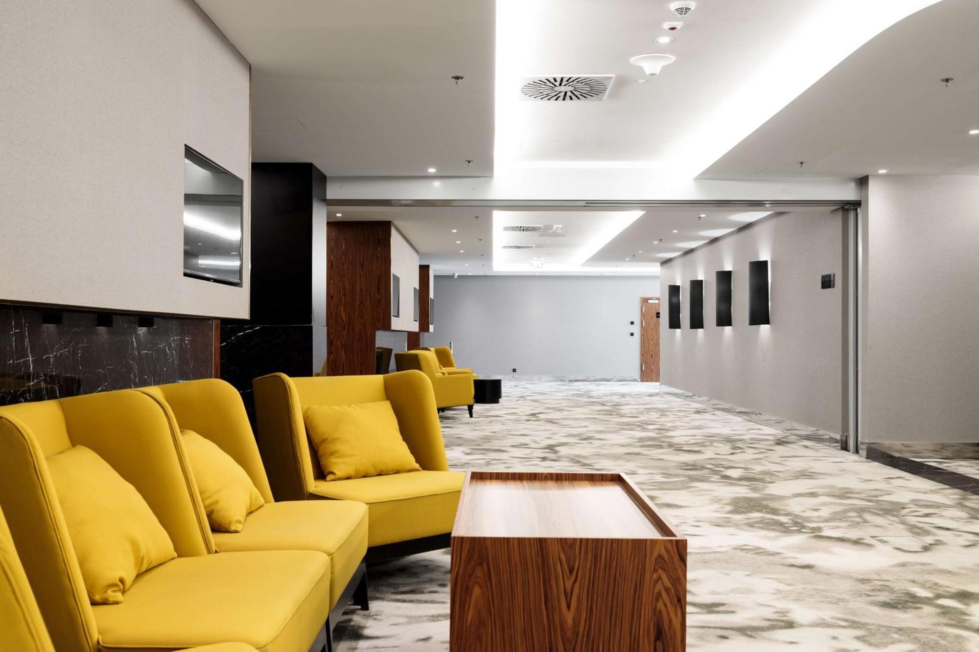Radisson Blu Resort 슈비노우이스쳬 외부 사진 The photo shows a modern interior space, likely a lobby or waiting area. There are several yellow sofas with cushions arranged in a casual seating area. In front of the sofas, there is a wooden coffee table. The flooring features a gray and white mar