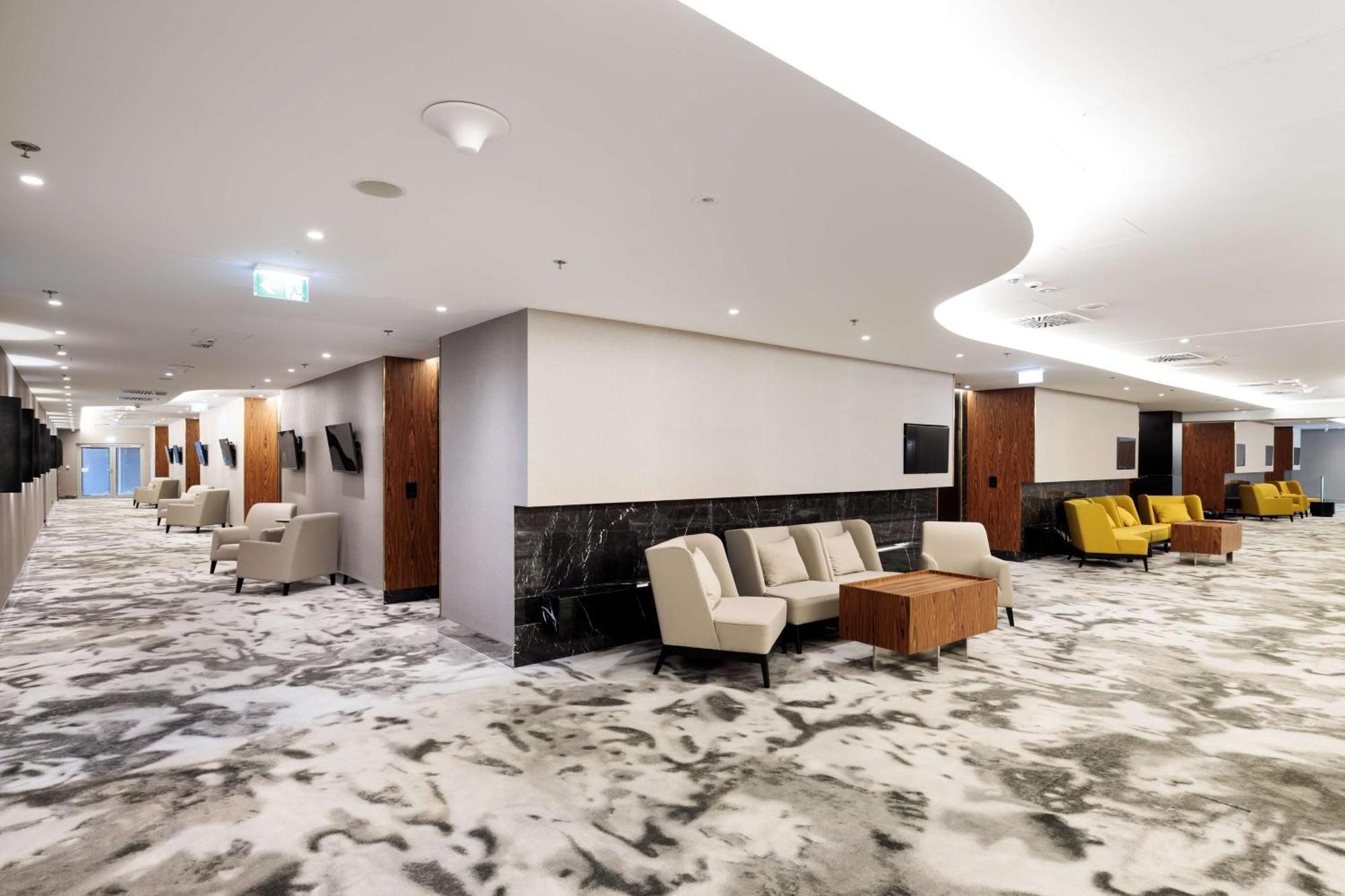 Radisson Blu Resort 슈비노우이스쳬 외부 사진 The photo shows a modern interior space, likely a lobby or lounge area. The flooring features a patterned carpet, and the walls are neutral in color, creating a calm ambiance. There are comfortable seating arrangements, including a group of beige cha