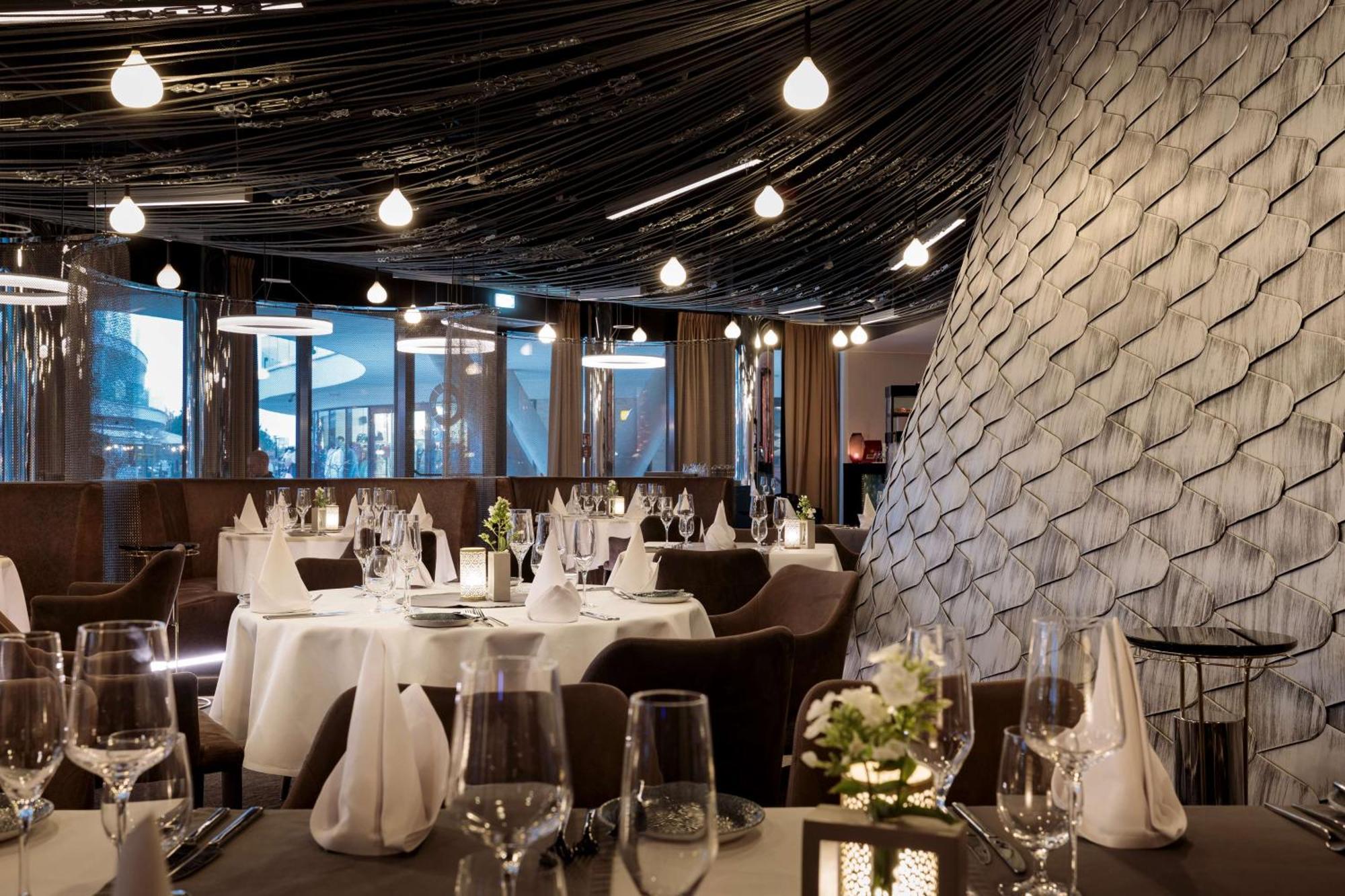 Radisson Blu Resort 슈비노우이스쳬 외부 사진 The photo shows a stylish restaurant interior. The dining area features elegantly set tables with white tablecloths, glassware, and folded napkins. There are decorative elements like small floral arrangements on the tables. The ceiling is adorned wit