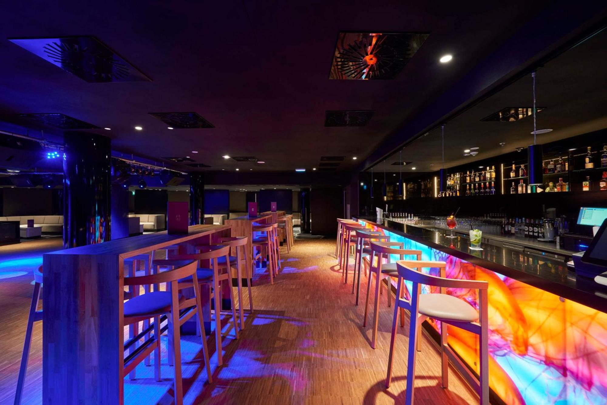 Radisson Blu Resort 슈비노우이스쳬 외부 사진 The photo depicts a modern bar interior with a sleek and contemporary design. There are high wooden stools positioned along a bar counter, which features vibrant, colorful lighting underneath. The bar area is dimly lit, creating a nightlife ambiance,