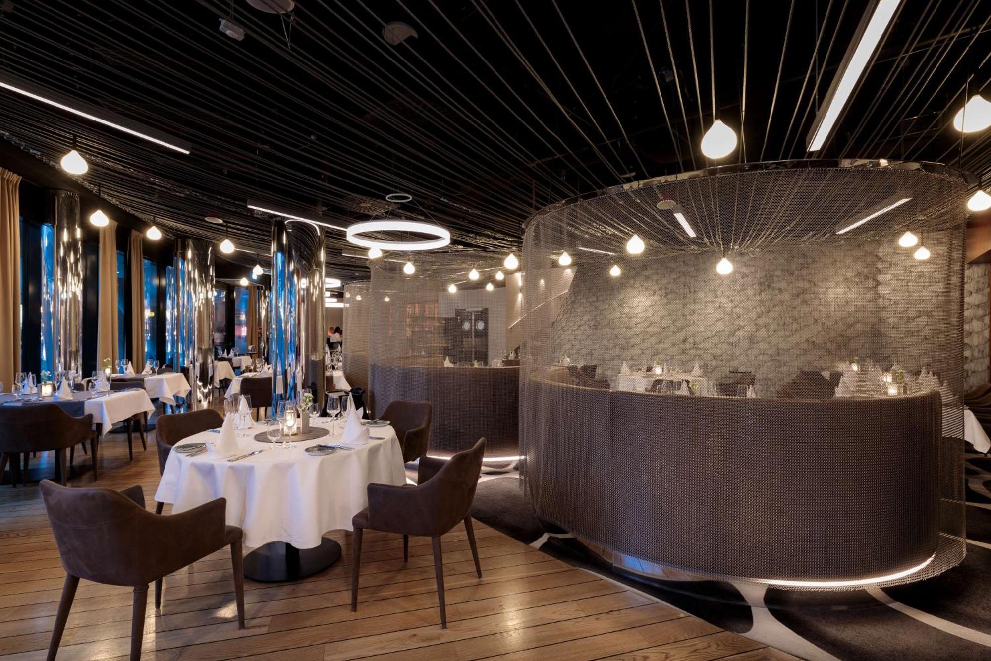 Radisson Blu Resort 슈비노우이스쳬 외부 사진 The photo shows an elegant restaurant interior. It features polished wooden floors and contemporary decor. Round tables are set with white tablecloths and have chairs arranged around them. The lighting is modern, with multiple pendant lights hanging 