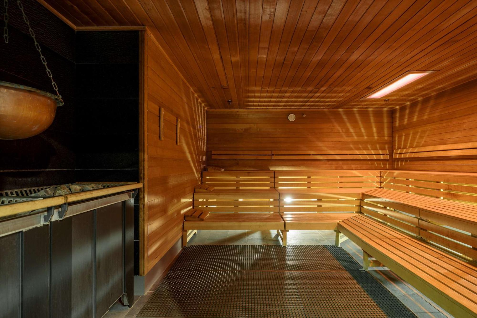 Radisson Blu Resort 슈비노우이스쳬 외부 사진 The photo shows the interior of a sauna. The walls and benches are made of wood, creating a warm and inviting atmosphere. There is a heater, likely for generating steam, and a metal rack connected to it, perhaps for holding stones or water. The desig