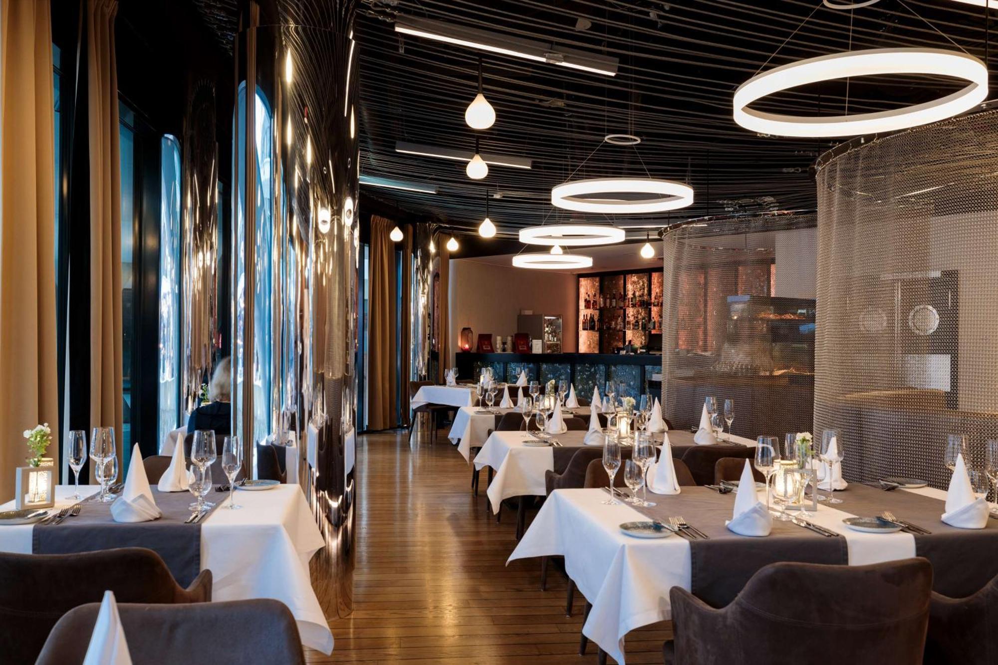Radisson Blu Resort 슈비노우이스쳬 외부 사진 The photo shows the interior of a modern restaurant. It features elegantly set tables with white tablecloths and neatly arranged glassware. The design includes a sleek, contemporary aesthetic with dark walls and interesting lighting, including circul