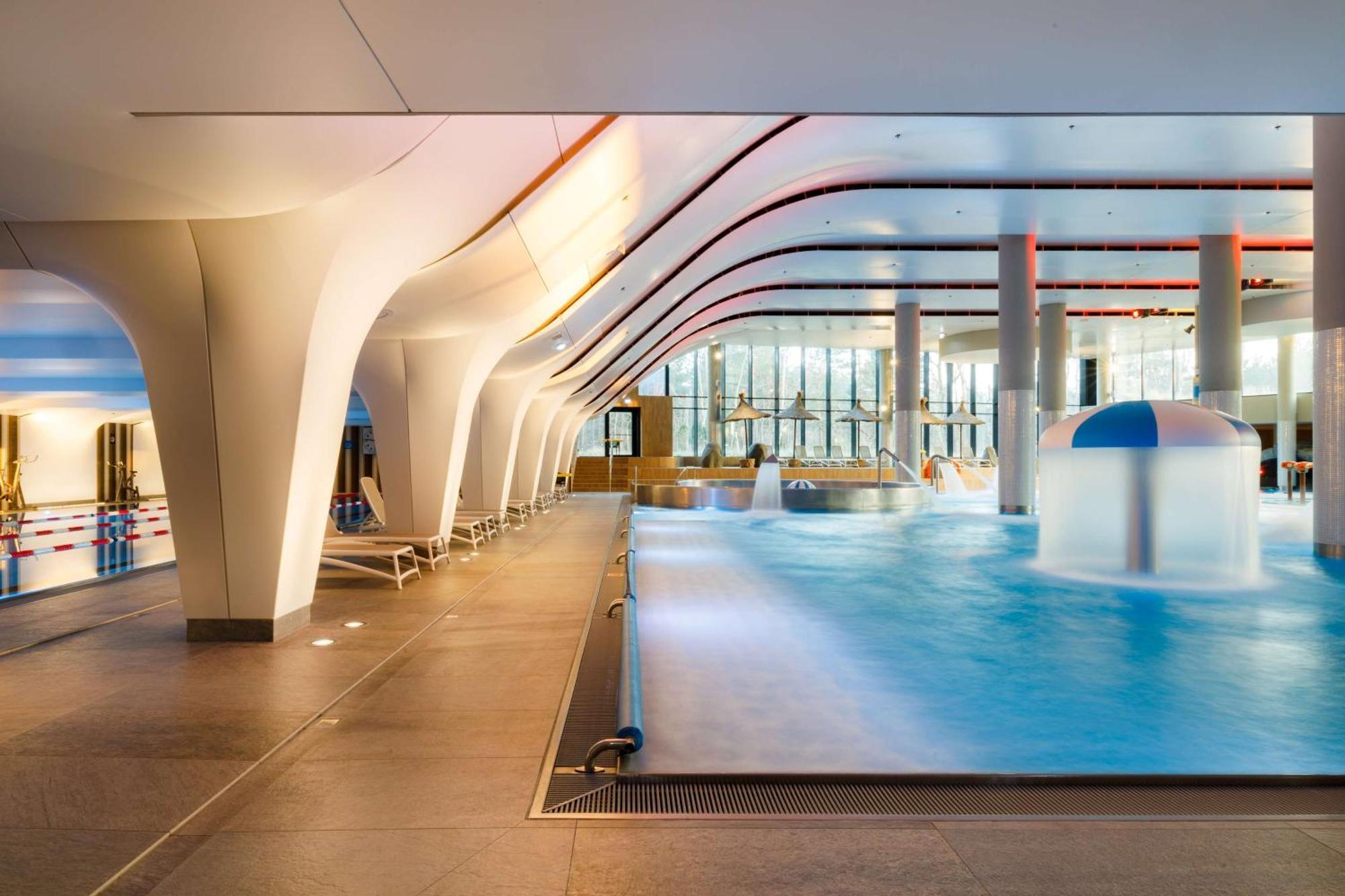 Radisson Blu Resort 슈비노우이스쳬 외부 사진 The photo shows an indoor swimming pool area with a modern architectural design. The space features large windows allowing natural light to enter, and the interior has smooth, flowing lines in the ceiling and columns. The pool has a light blue water 