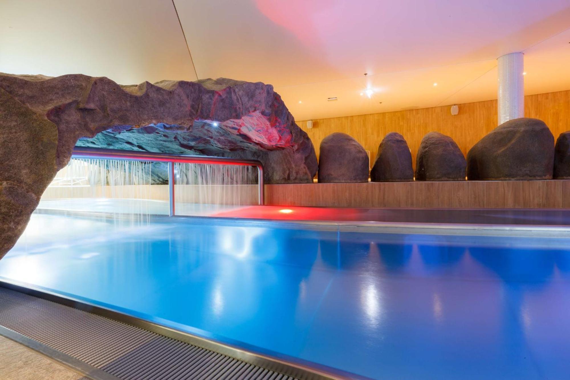 Radisson Blu Resort 슈비노우이스쳬 외부 사진 The photo shows a serene indoor swimming pool area. The pool has clear blue water, and there is a distinctive rock formation that resembles a cave on one side. Soft lighting enhances the atmosphere, casting a gentle glow across the space. In the back